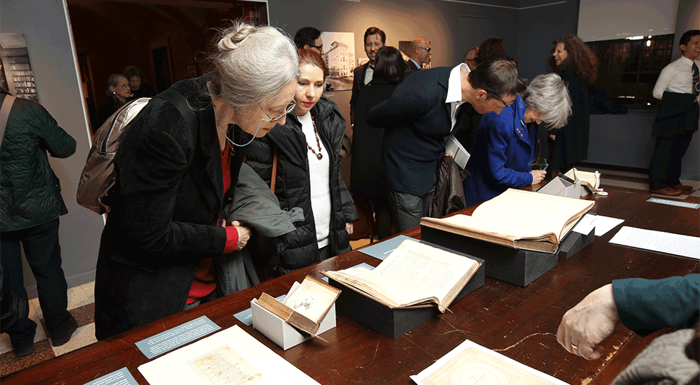 Guests lean over a long table to review the documents, books, and artifacts about the early development of the Casa Italiana.