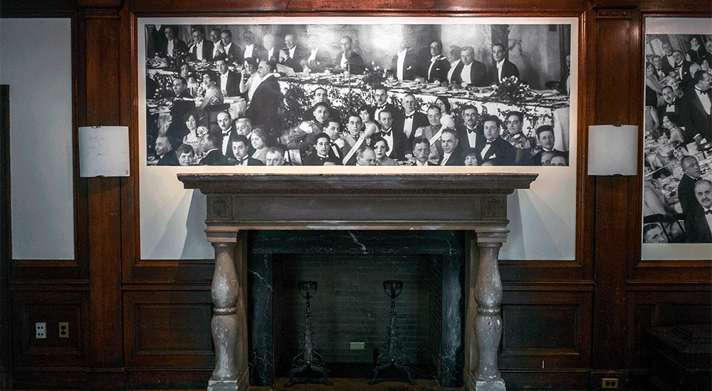 Photo close-up of the fireplace with a historical photo above the mantelpiece showing the 1927 inauguration dinner for the Casa Italiana.